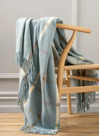 Light blue check lambswool fringed throw draped across wooden chair